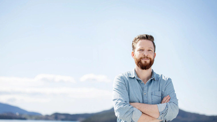 Utendørs portrett av forfatter Anders Totland i en hverdagsskjorte med armene i kryss. Halvportrett av forfatteren i forgrunnen, bakgrunnen viser et havlandskap ute av fokus.