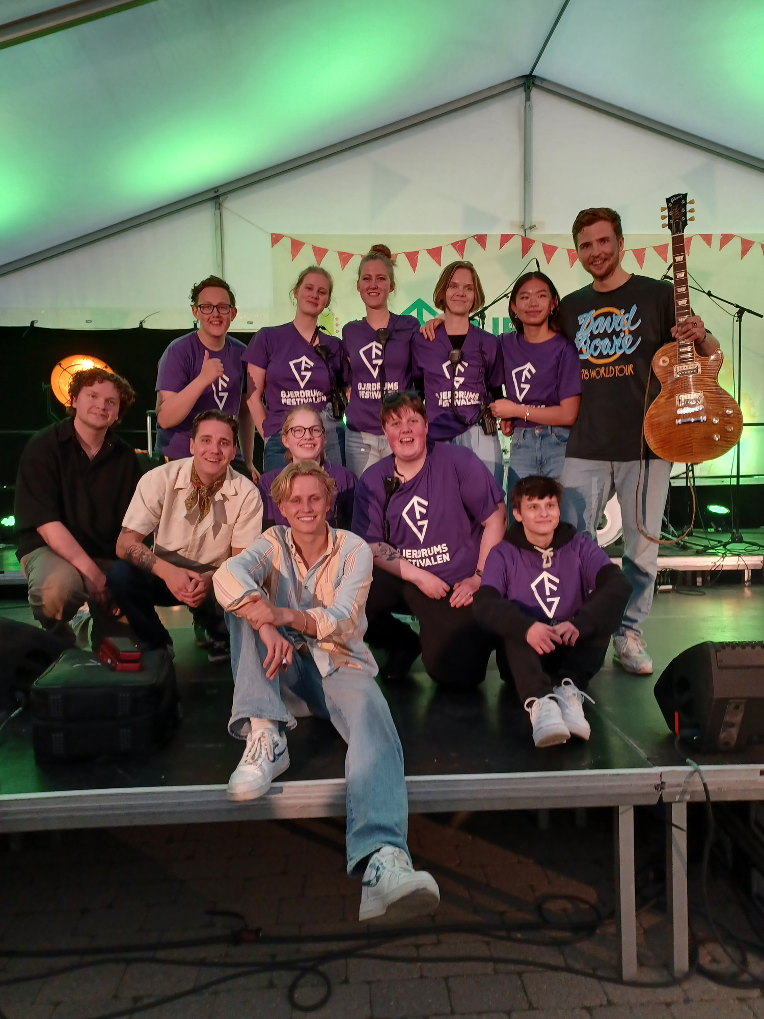 Bildet viser ungdommene i unge arrangører som står oppstilt på scenen med festival t-skjorter rundt artisten og bandet Bølgen etter gjennomført ungdomskonsert.